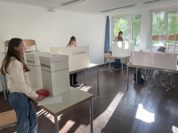 Schueler:innen wählen, im Klassenzimmer steht eine Urn